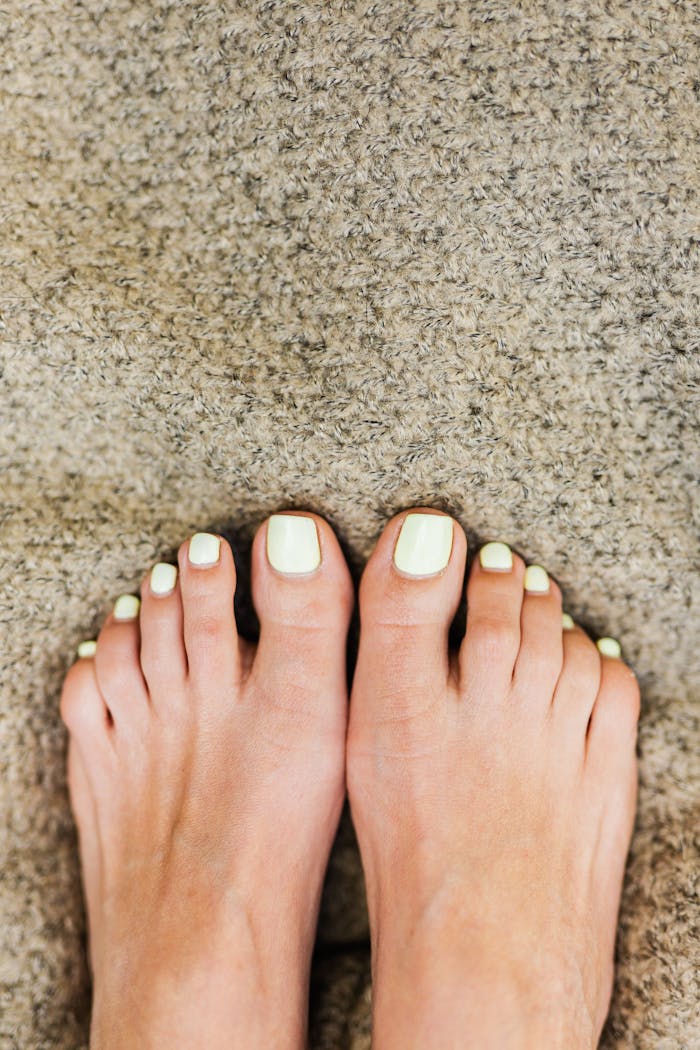 Close-up of bare feet with light green nails on a textured carpet.